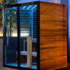 VATRA 3-4 PERSON SAUNA showcasing the deep red cedar exterior, blue chromotherapy lights and glass side